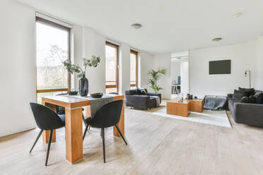 Bequeme graue Sofas in der Nähe von Tisch auf Teppich in hellem stilvollen Wohnzimmer mit Fenstern und grüner Topfpflanze in Villa platziert - ADSF35175