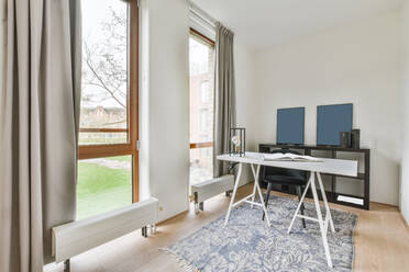 White table with opened book placed on rug near windows in light spacious home office with decorative frames in flat - ADSF35183