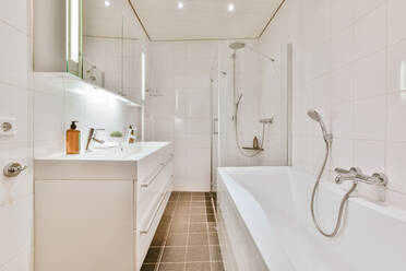 Keramische Badewanne vor dem Waschbecken in einem hellen, stilvollen Badezimmer mit Glasduschkabine und weiß gefliesten Wänden - ADSF35187