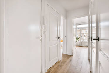 Empty narrow hallway with white walls and doors and wood laminated floor in house - ADSF35189