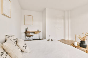 Comfortable bed with white sheets placed in light spacious bedroom with chair at table near decorative frame - ADSF35199