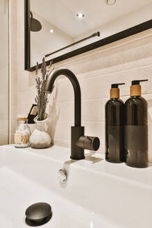 Nahaufnahme eines Waschbeckens mit einem schwarzen Wasserhahn, einem Spiegel und verschiedenen dekorativen Elementen auf dem Waschbecken. - ADSF35206