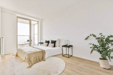 Comfortable bed with blanket in light bedroom with parquet floor and bedside table placed near windows in modern apartment - ADSF35223