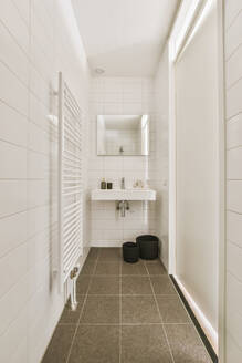 Weißes Waschbecken unter Spiegel in hellem Badezimmer in Wohnung mit Handtuchtrockner - ADSF35225