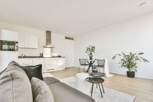 Interieur einer geräumigen, modernen Wohnung im minimalistischen Stil mit offener Küche und bequemen Sofas am Esstisch im Tageslicht - ADSF35230