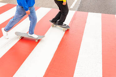 Crop view of two faceless friends skaters wearing blue and yellow sweaters skating by a zebra crossing - ADSF35268