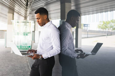 Seitenansicht eines afroamerikanischen männlichen Unternehmers in formeller Kleidung, der auf einem Netbook tippt, während er in der Nähe eines Bürogebäudes in der Stadt steht - ADSF35274