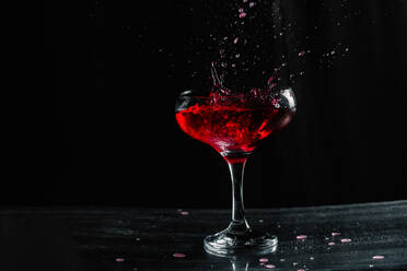 Spritzen leckeren alkoholischen Rotwein mit kleinen Tropfen in transparenten Weinglas auf dem Tisch vor schwarzem Hintergrund in modernen Studio platziert - ADSF35318