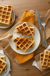 Von oben leckere hausgemachte süße gebackene Waffeln, die auf einem Schneidebrett in der Nähe der Schöpfkelle auf einem Holztisch in einer hellen Küche serviert werden - ADSF35319