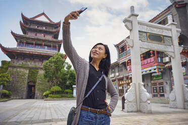 Asian young woman doing a selfie with smartphone in Chinese traditional town during trip - ADSF35320