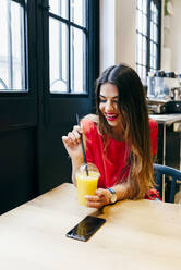 Beautiful smiling modern female enjoying fruit juice while sitting at wooden table in cafe - ADSF35326