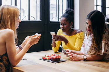 Junge verschiedene weibliche Freunde, die lustige Videos auf dem Smartphone anschauen, während sie den Morgen in einem kleinen Café verbringen und zusammen gesund frühstücken - ADSF35330
