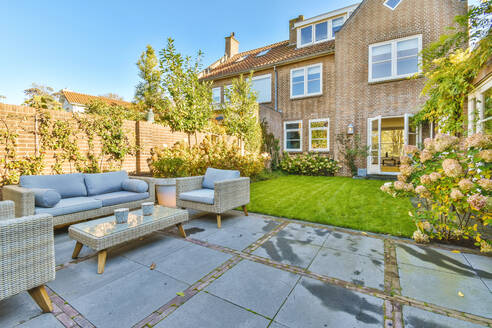 Terrasse eines Wohnhauses mit grünem Rasen und Sofas auf einem Tisch auf gefliestem Boden an einem Sommertag in einem Vorort - ADSF35371