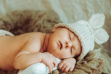 Adorable lustige neugeborenes Baby in gestrickte Mütze und Höschen mit Hasenohren und Schwanz liegen auf weichen Pelz karierten ad schlafen im Tageslicht - ADSF35445