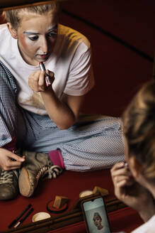 From above young professional female mime in casual clothes painting lips and looking in mirror in dressing room - ADSF35459