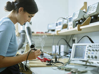 Lächelnder Techniker mit Arbeitsgerät beim Löten elektronischer Geräte am Schreibtisch im Labor - CVF01986