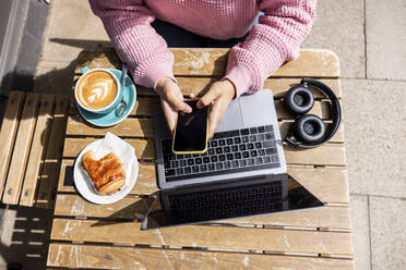 Woman using mobile phone sitting at sidewalk cafe on sunny day - WPEF06053