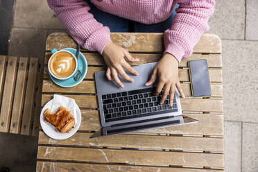 Young woman using laptop sitting at sidewalk cafe - WPEF06054