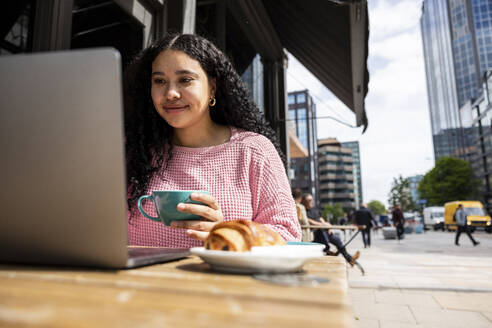 Lächelnde Frau mit Kaffeetasse und Laptop in einem Straßencafé - WPEF06057