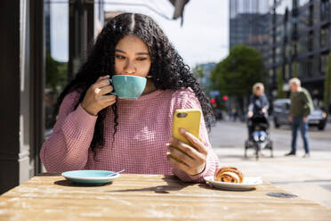 Junge Frau trinkt Kaffee und benutzt ihr Smartphone in einem Straßencafé - WPEF06061