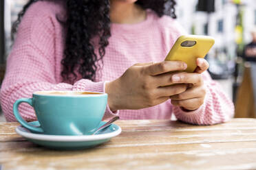 Junge Frau Textnachrichten über Handy sitzend mit Kaffeetasse st Bürgersteig Café - WPEF06066