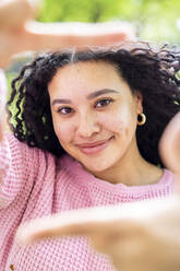 Smiling woman with curly hair making finger frame - WPEF06069