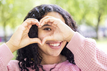 Happy woman gesturing heart shape in front of eye - WPEF06071