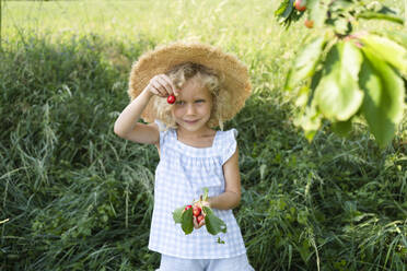 Smiling girl wearing hat holding cherry at field - SVKF00300