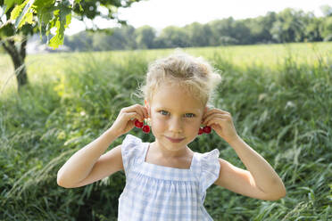 Smiling cute girl wearing cherry earring at field - SVKF00302