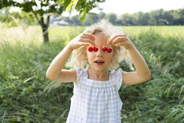 Blond girl covering eyes with cherries - SVKF00303