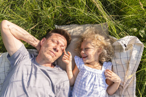 Glückliches Mädchen mit Vater auf Picknickdecke im Gras liegend - SVKF00313