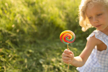 Girl holding rainbow lollipop on sunny day - SVKF00319