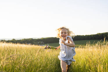 Fröhliches Mädchen läuft auf einem Feld an einem sonnigen Tag - SVKF00323