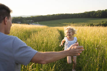 Cheerful blond girl running towards father at field - SVKF00326