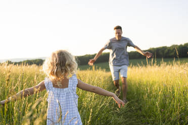 Mature man running towards daughter standing with arms outstretched at field - SVKF00329