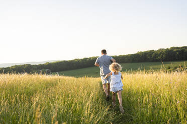 Father and daughter running together in field - SVKF00330