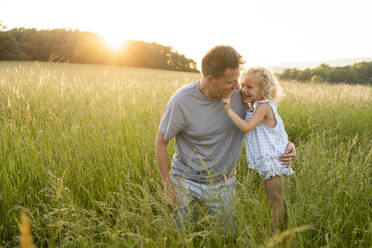 Happy girl standing by father kneeling on grass at field - SVKF00333