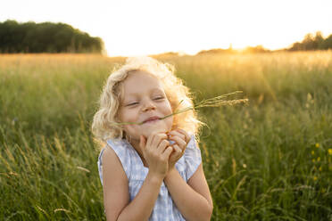 Lächelndes blondes Mädchen mit Gras im Mund genießt auf dem Feld - SVKF00340