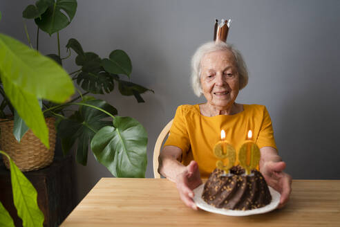 Lächelnde ältere Frau feiert Geburtstag mit Kuchen zu Hause - SVKF00358