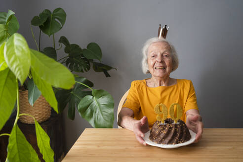 Glückliche ältere Frau feiert Geburtstag mit Kuchen zu Hause - SVKF00359