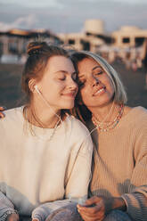 Smiling mother and daughter with eyes closed enjoying music through in-ear headphones - OMIF00921