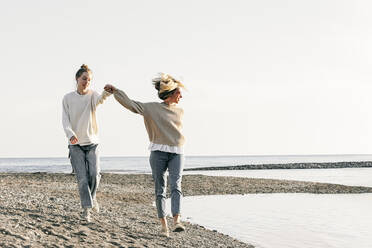 Mutter und Tochter halten sich an den Händen und gehen zusammen am Strand spazieren - OMIF00926