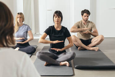 Mann und Frauen sitzen auf Übungsmatten und machen Entspannungsübungen in einem Yogastudio - JSRF02135