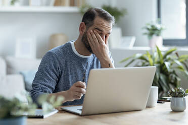 Erschöpfter Geschäftsmann sitzt mit Laptop im Home Office - JSRF02143