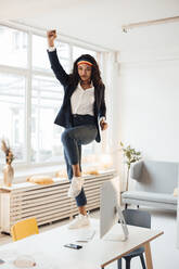 Businesswoman dancing on desk in office - JOSEF10722