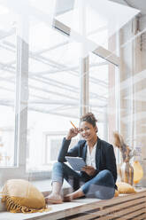 Happy businesswoman with digital tablet PC sitting in front of window - JOSEF10726