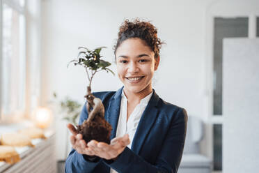 Glückliche Geschäftsfrau mit Pflanze im Büro - JOSEF10730