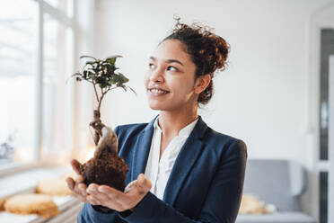 Smiling businesswoman with plant in office - JOSEF10731