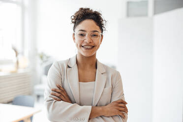 Happy businesswoman wearing eyeglasses standing in office - JOSEF10763