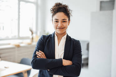 Smiling businesswoman with arms crossed standing in office - JOSEF10764